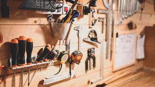 wooden wall with tools hung on racks, in tubs, on hooks
