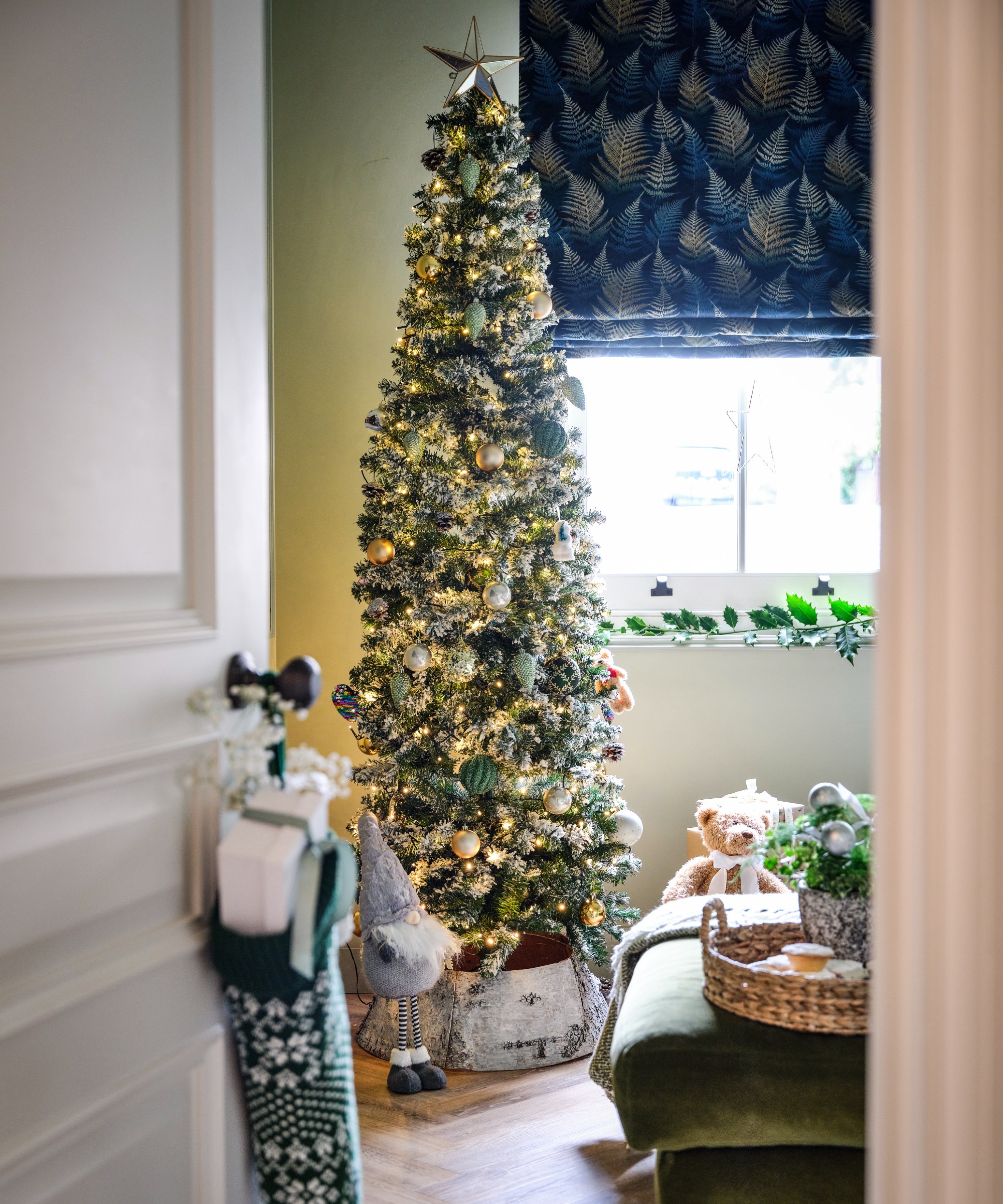 A slim space-saving Christmas tree fully decorated in a living room