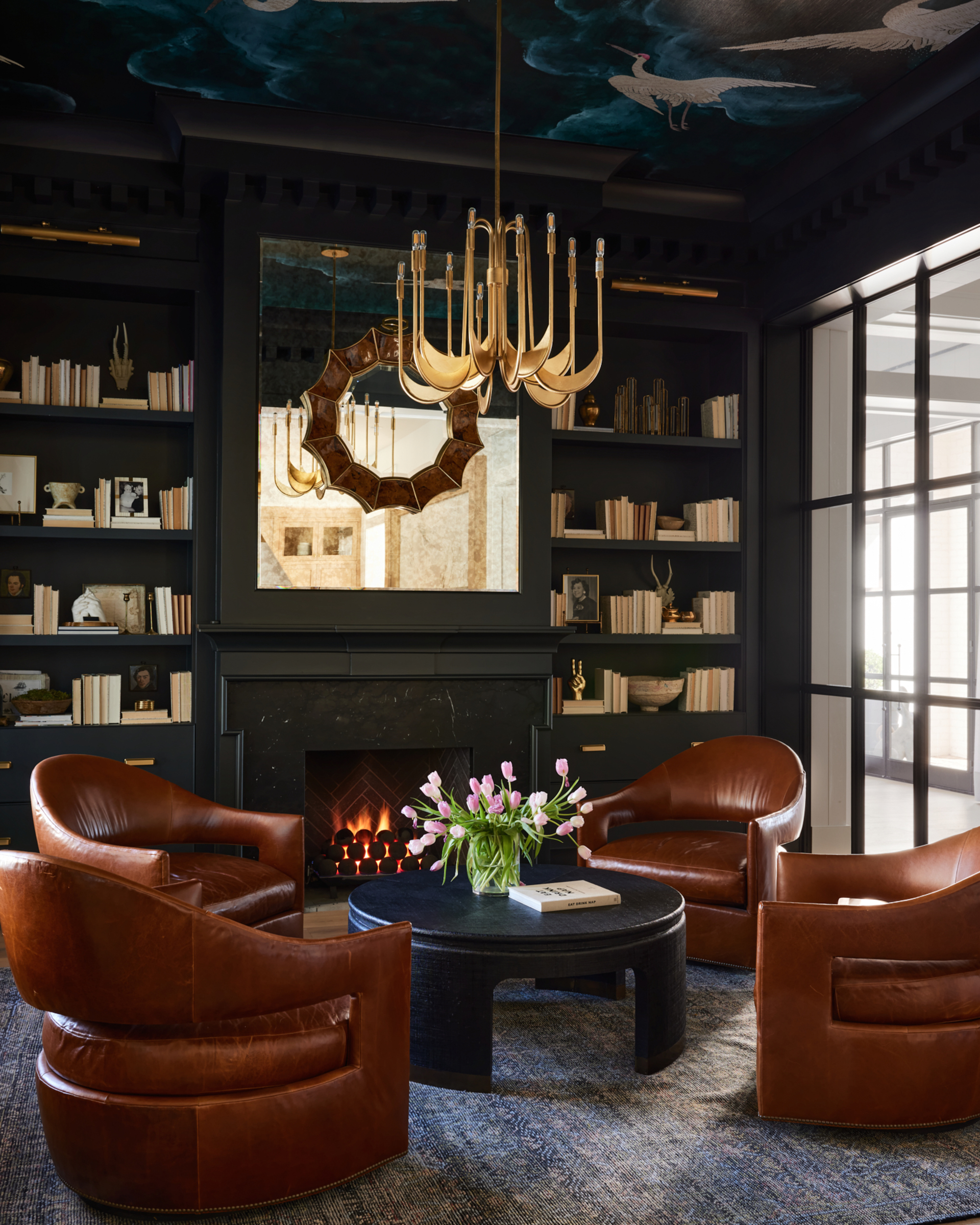 A living room with a moody palette, built-in bookshelves, and four leather accent chairs around a circular coffee table