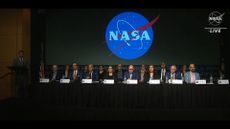 A group of people seated at a table in front of a NASA logo.