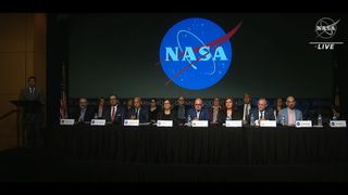 A group of people seated at a table in front of a NASA logo.