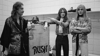Rush pose next to a flight case backstage in Springfield, Massachusetts, 9th December 1976 during their All The World's a Stage tour.