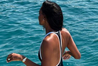 Woman wearing black and white one-piece bathingsuit on background of blue water.