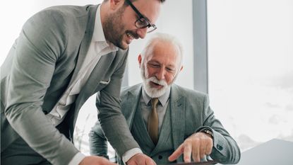 Two executives, a father and a son, look over some paperwork together.