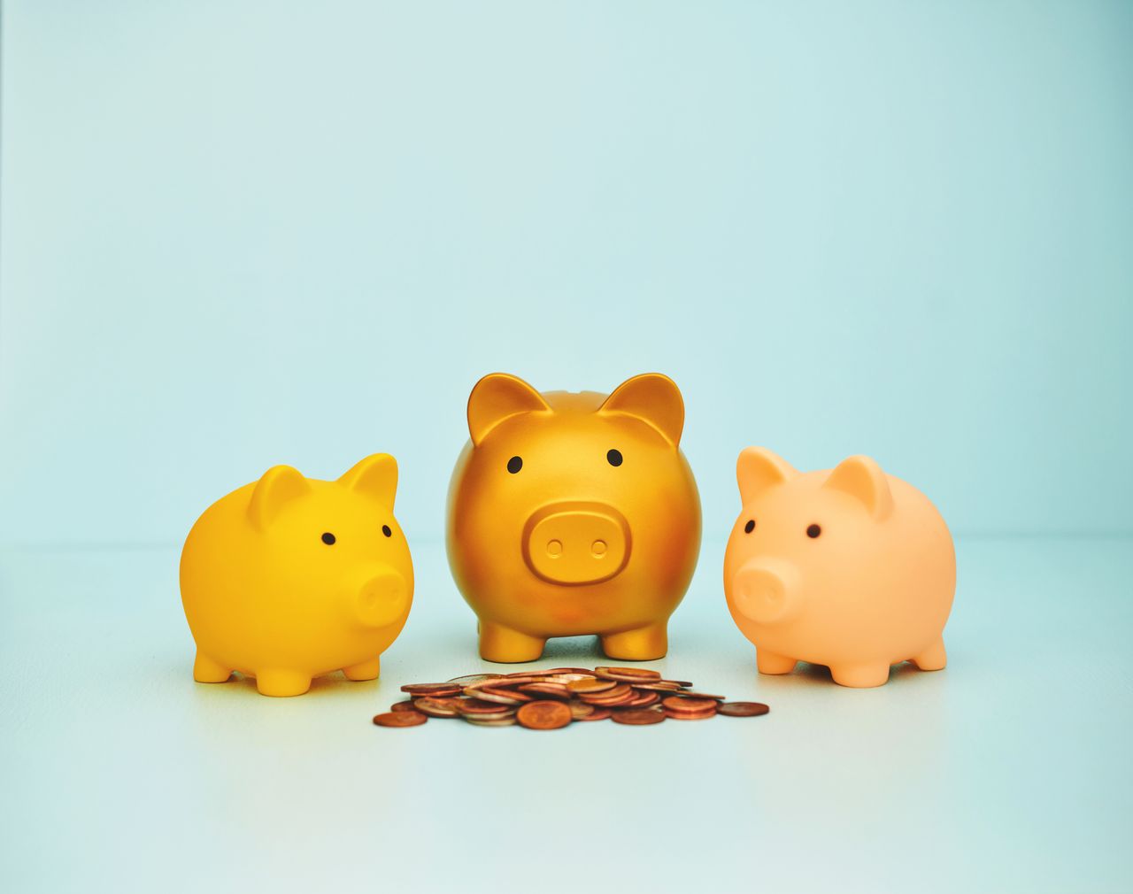 Row of three piggy banks behind a stack of coins. 