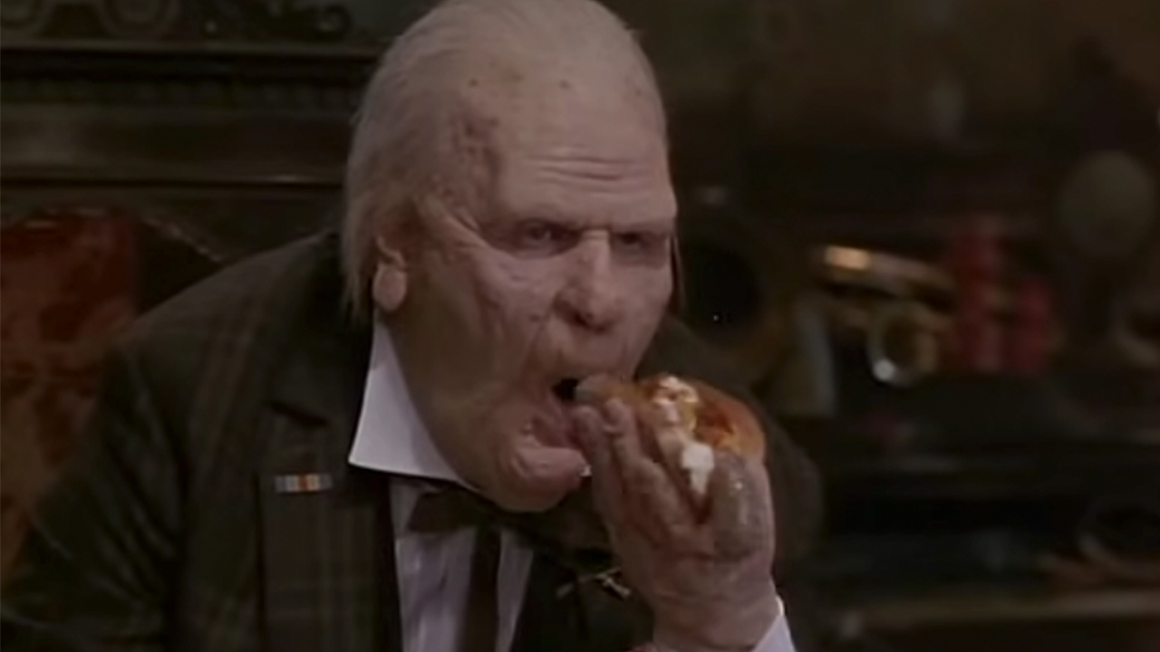 Dan Aykroyd with heavy makeup, looking like a very old man, eating a hot dog in Nothing But Trouble