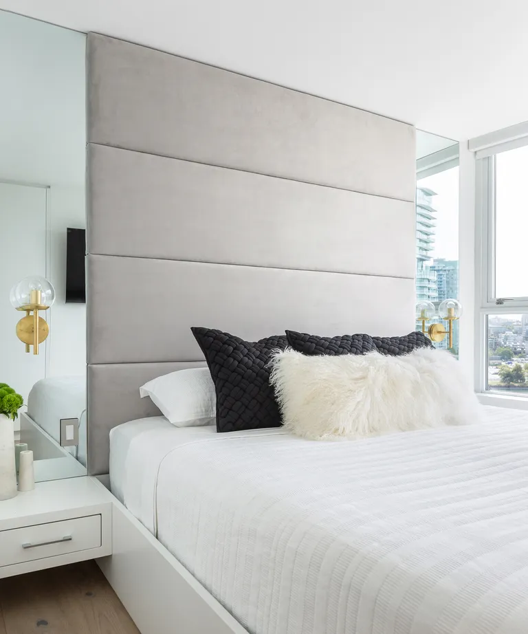 An apartment bedroom with mirrored panels on either side of the bed, reflecting the window view