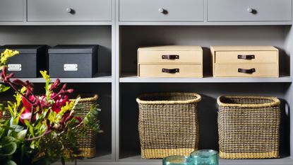 Grey painted shelving unit with baskets, books, television and ornaments painted the same colours as a grey wall