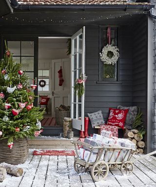 Christmas porch decor ideas with black shiplap walls, a full Christmas tree, seating area with cushions and a sled