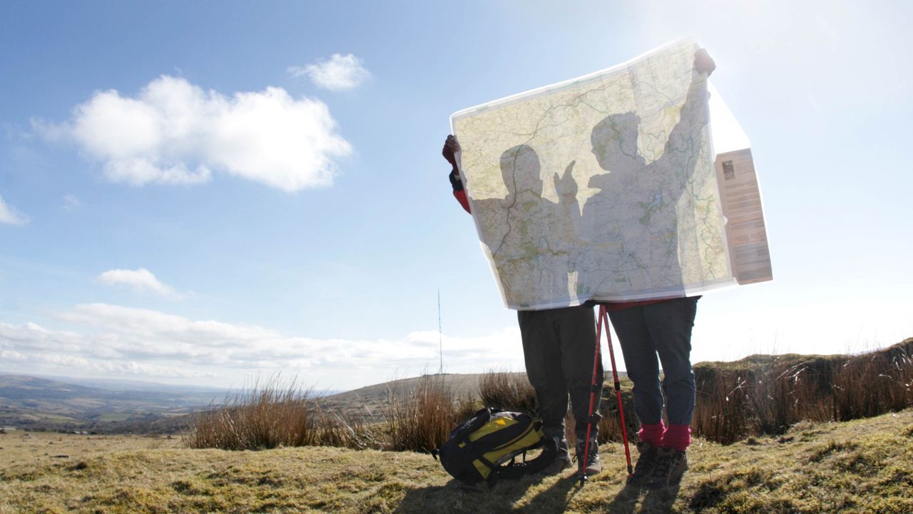 Two hikers look at a map on a sunny day.