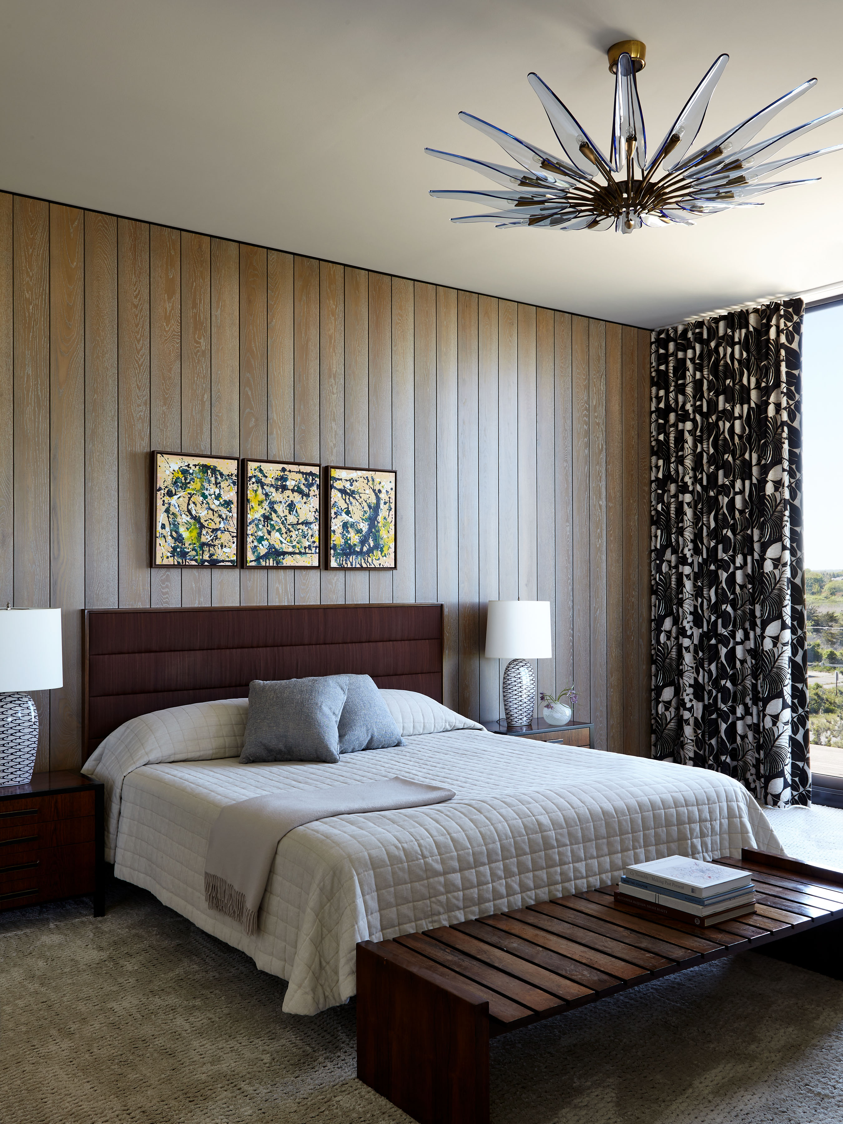A minimalist bedroom with wood paneled walls employs a maximalist black and white drape for contrast and balance.