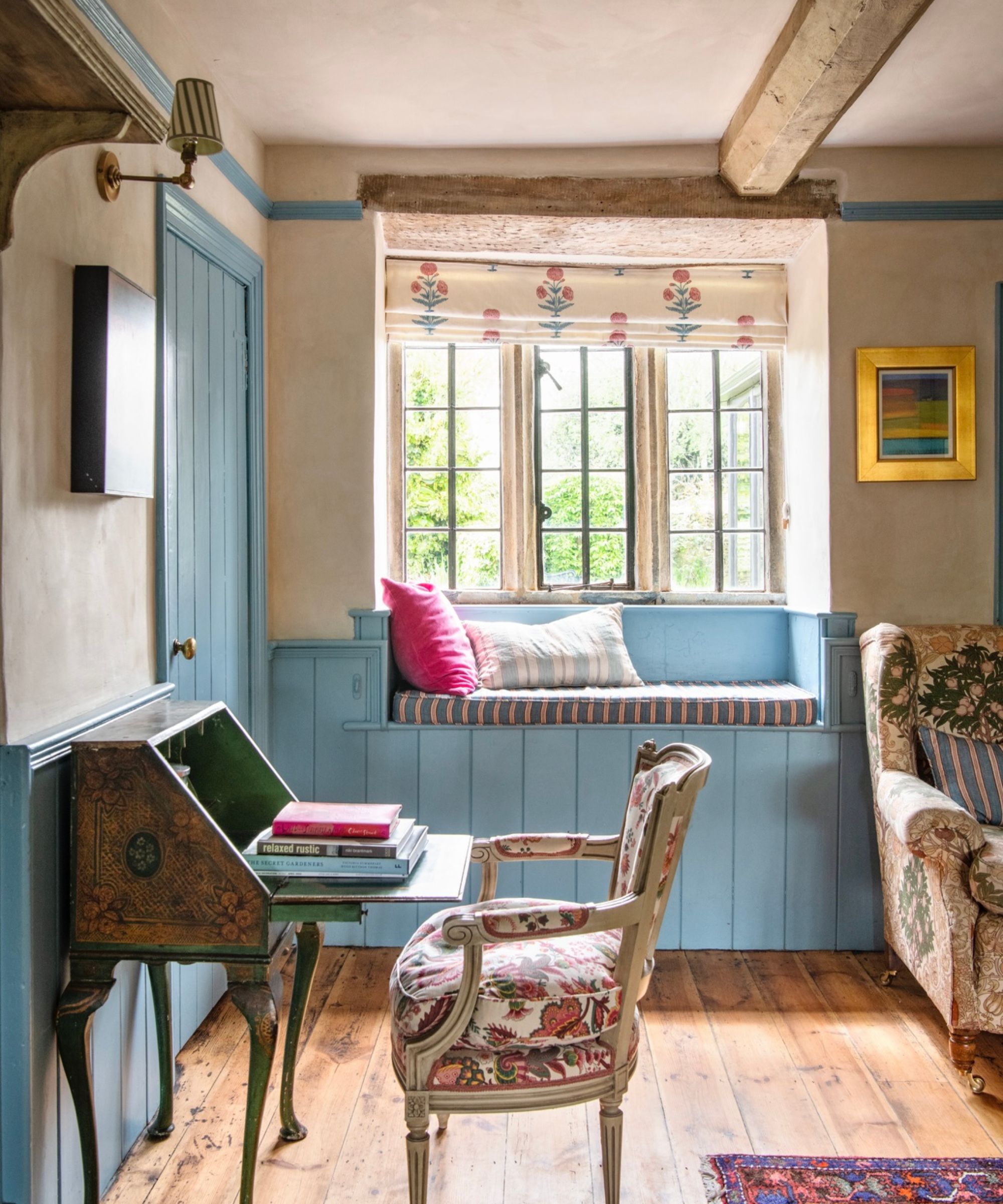 A rustic living room with wood ceiling beams, a window with a window seat, and blue paneling.