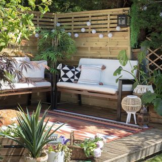 raised deck area in corner of garden with fencing screen string lights orange stripe outdoor rug and white and wood outdoor sofas