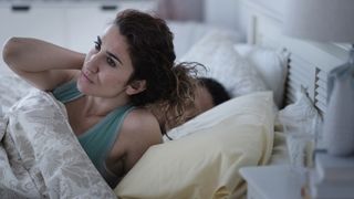 A woman with long brown hair holds her sore, painful neck in bed
