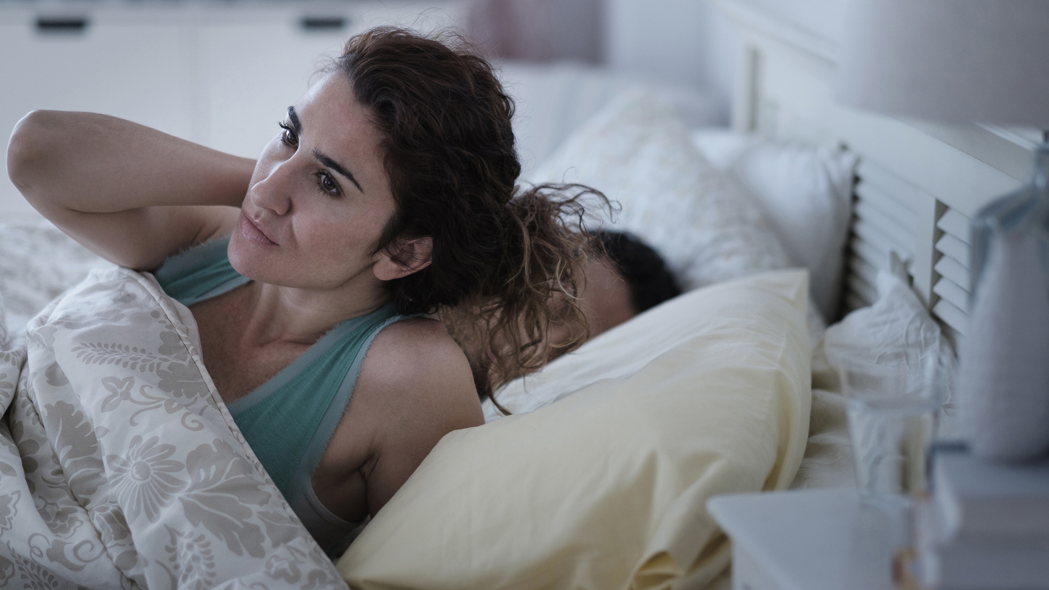 Seorang wanita dengan rambut coklat panjang memegangi lehernya yang sakit dan sakit di tempat tidur