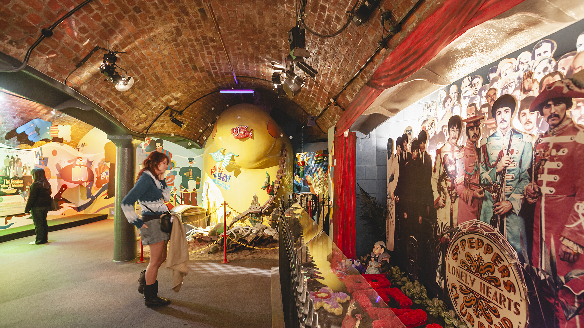 A girl listen to the audio guide while visiting the Beatles Story Museum at Royal Albert Dock with the reconstruction of the Yellow Submarine title of a famous Beatles song in the background.