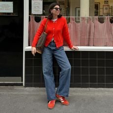 Woman on street wears red cardigan, blue jeans, red trainers