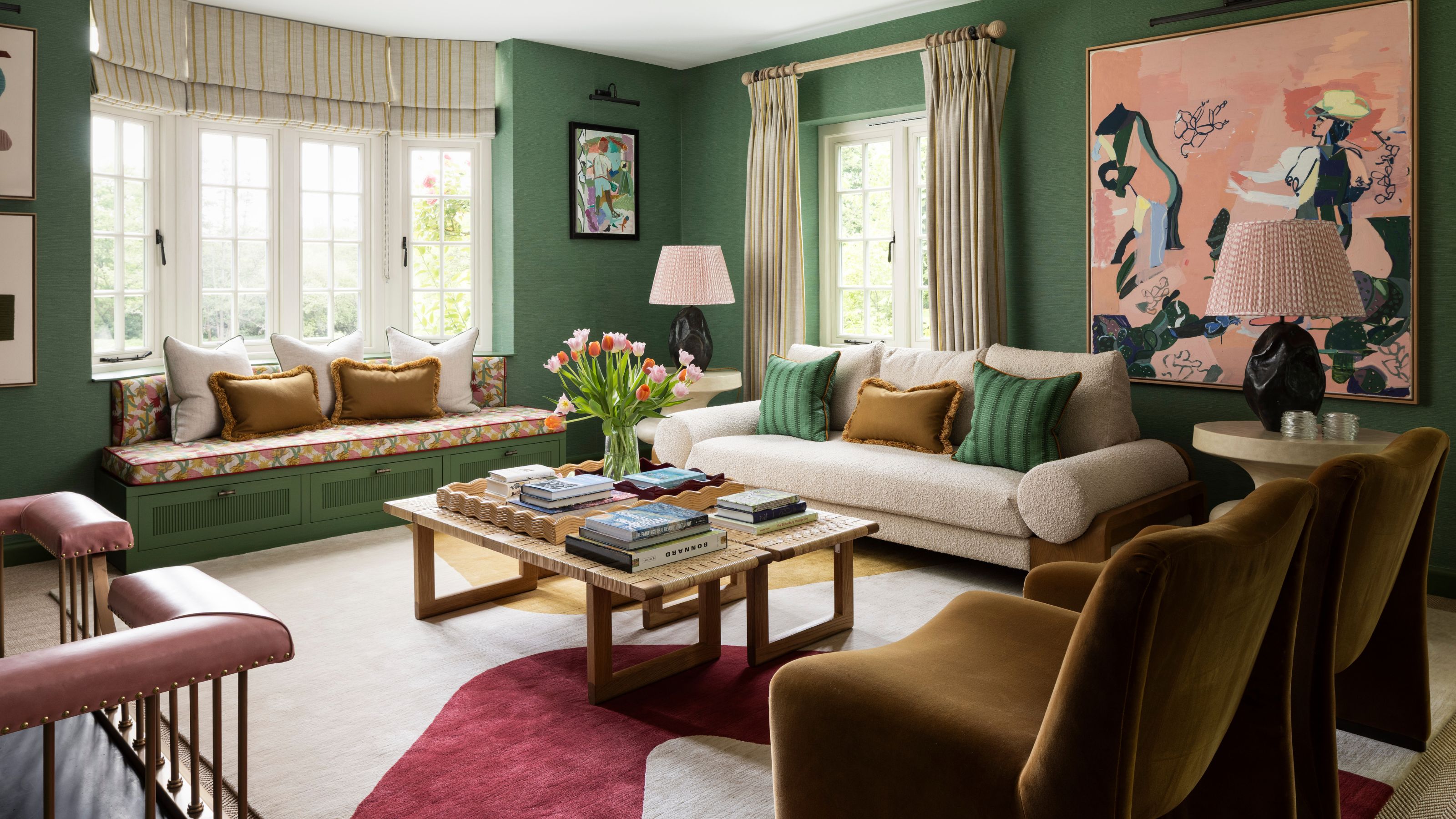 a rich green drawing room with a bay window, window seat, neutral couch, two velvet chairs and a large pink cowboy themed art piece