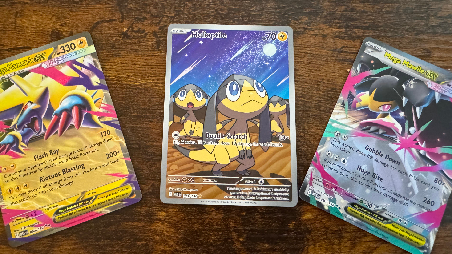 Three Pokemon TCG Mega Evolution cards laid out on a wooden surface