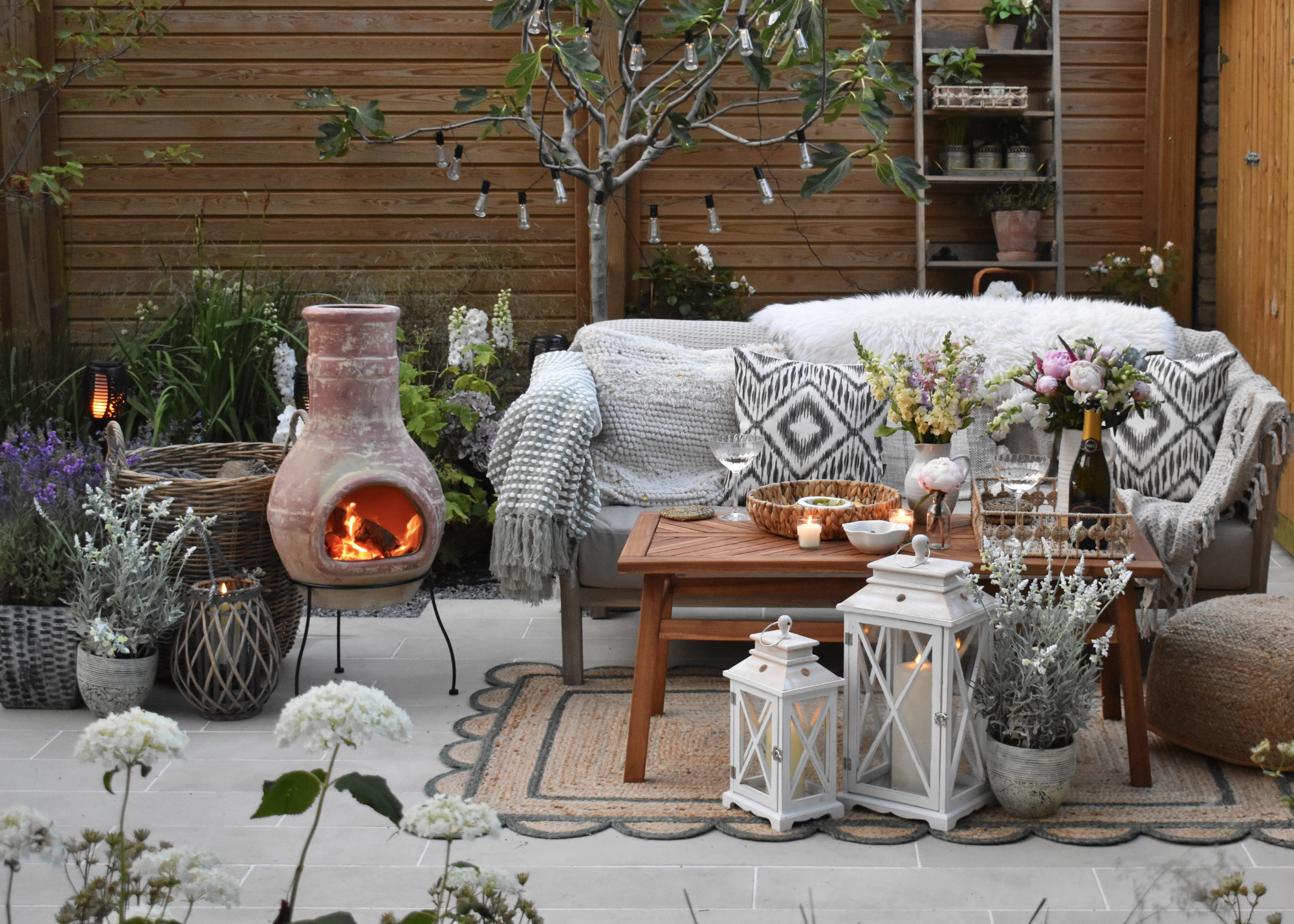 fall backyard ideas with chiminea, blankets, and cushions with candles and plant pots also scattered around