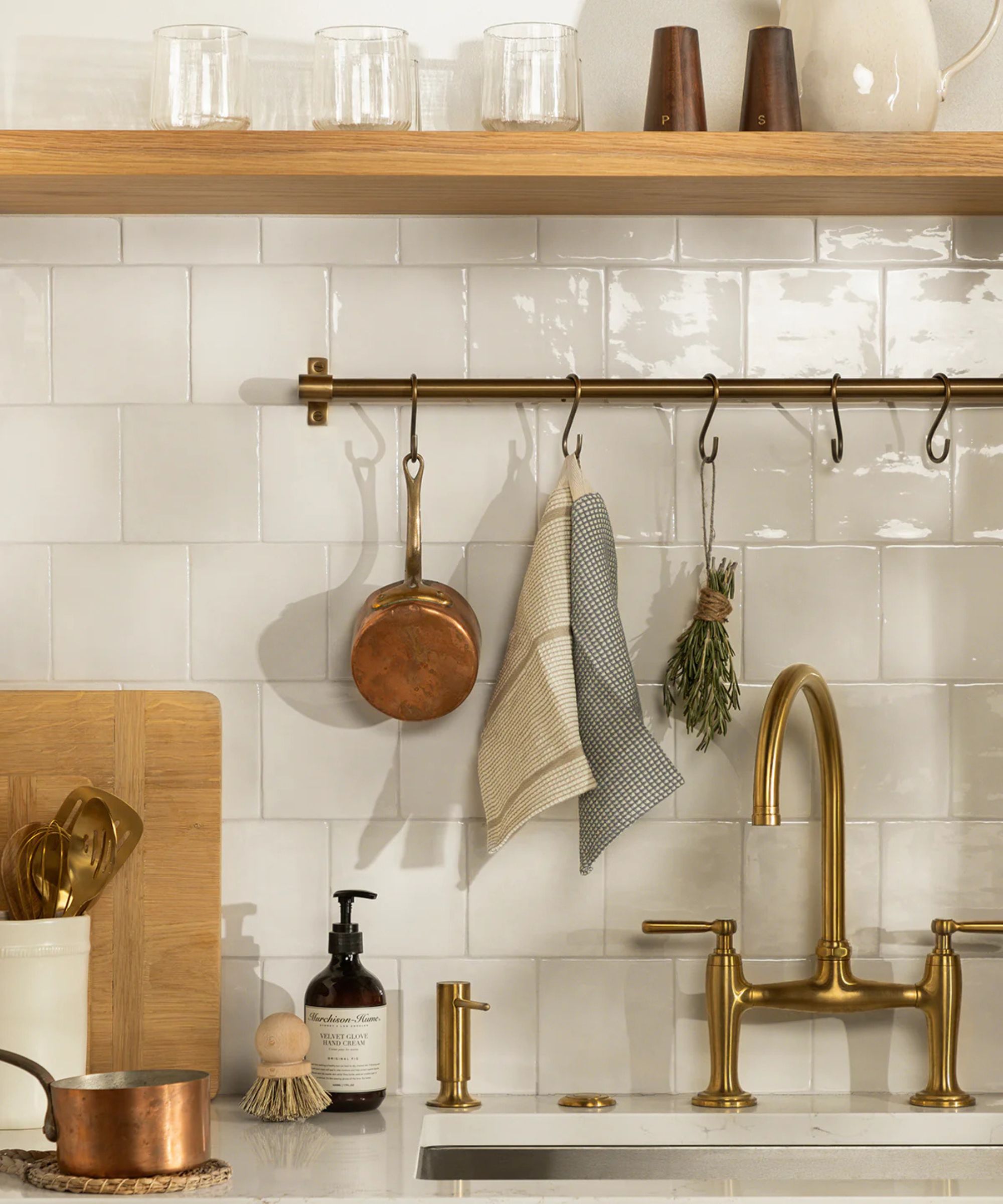White tiled backsplash with pot rail and copper pot hanging and gold tap