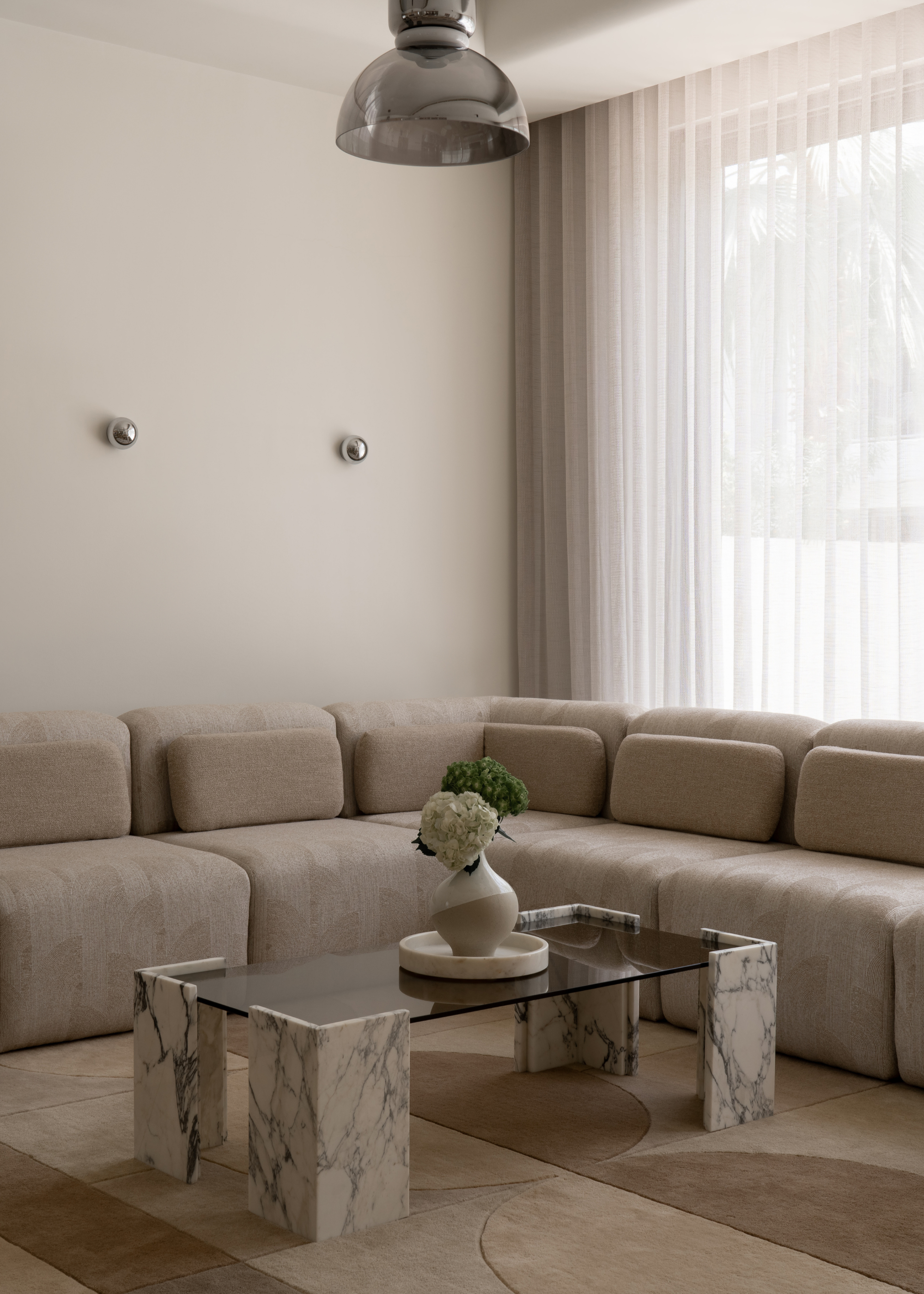 A minimalist living room with a cozy pale brown sofa, a marble coffee table, a geometric area rug, and a black glass pendant light