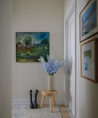 white entryway with blue and green artwork and wooden stool with flowers on