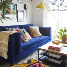 Four cushions and a creamy mustard throw on top of blue couch next to coffee table with shelves and reading material