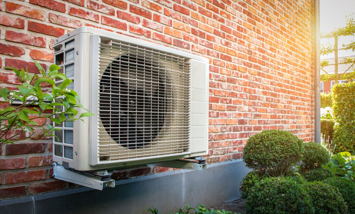 A heat pump affixed to an exterior brick wall