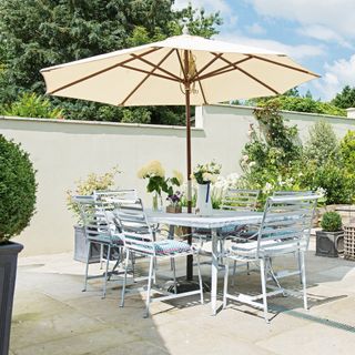 Paved patio with white painted garden wall and a dining table with cream parasol