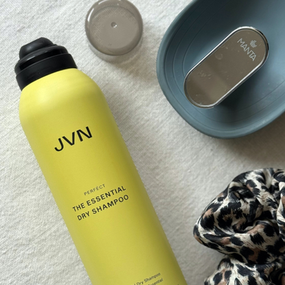 Bird's eye view of JVN Hair The Essential Dry Shampoo without its lid, a slate blue Manta Hair Brush and a leopard print scrunchie, set on an off-white linen background