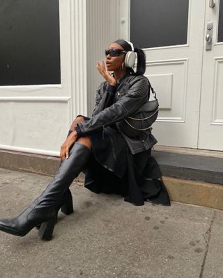 Woman wearing black skirt, leather jacket, and tall black boots.