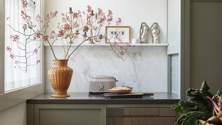 a countertop in a green kitchen with a vase, branch, toaster and pie on