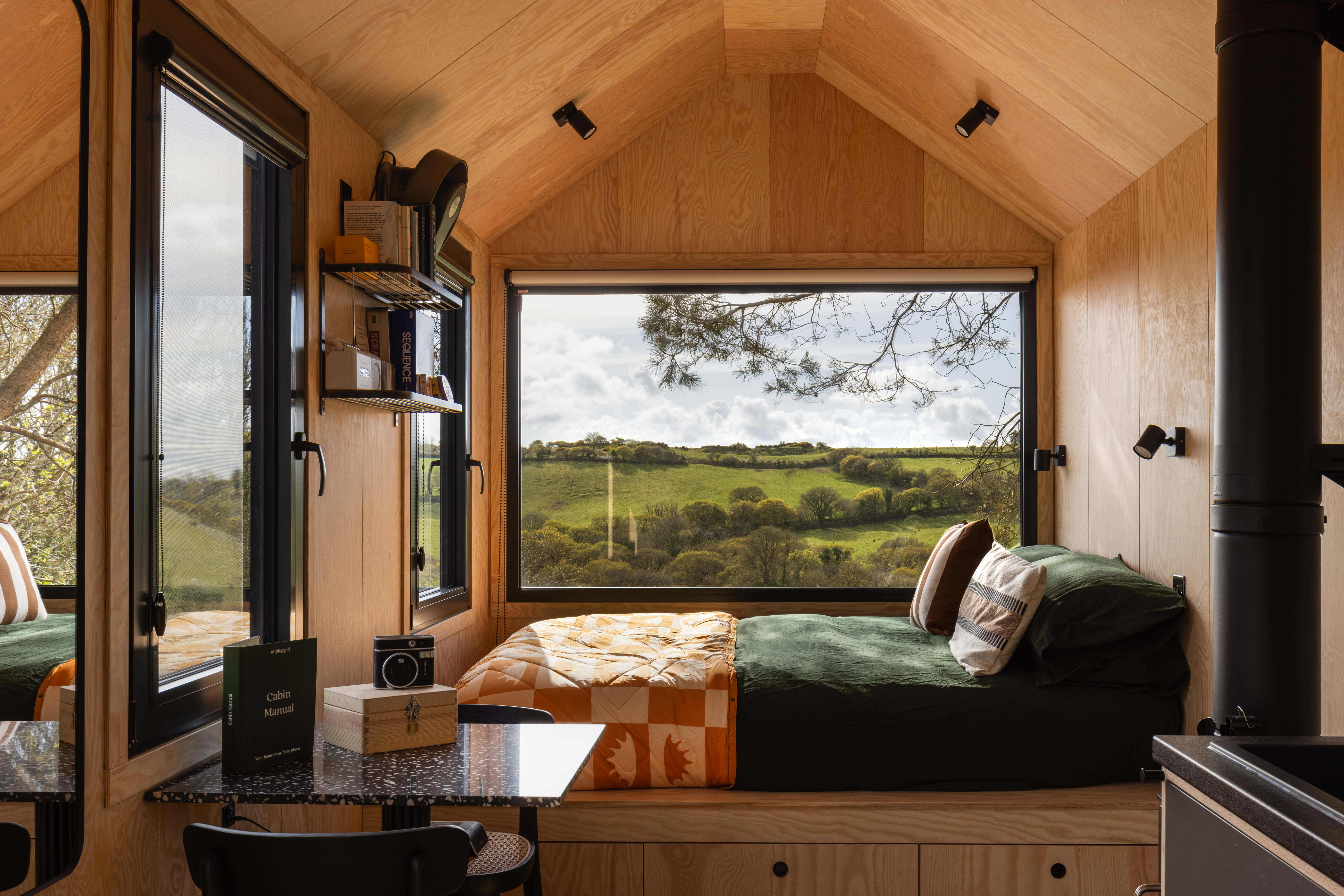 Light wood cabin interior with a built-in bed, small table and wood-burning stove
