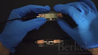 a person with gloved hands holds a small battery