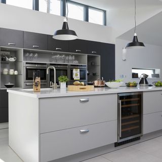 grey island with fridge and grey drawers, dark grey cabinets with white walls and black pendant lights