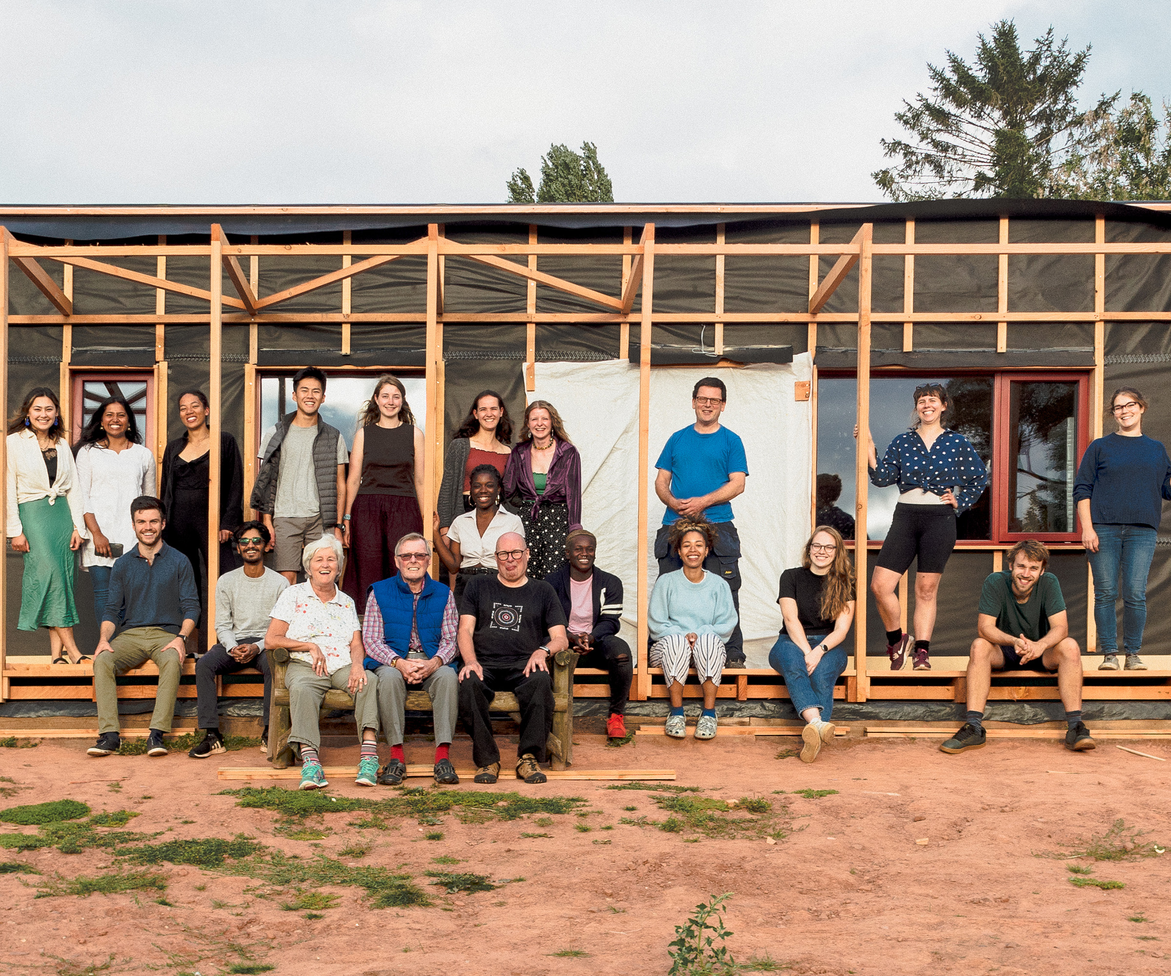 Team of young trainee builders standing together in front of a half-finished shell of a self build home that they are all working on
