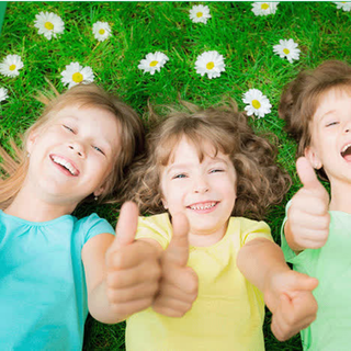Three children pictured lying on the grass with their hands in a thumbs up gesture, smiling