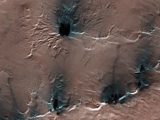 Strange spider-like features creep on the surface of Mars in this image taken by the High-Resolution Imaging Science Experiment (HiRISE) camera on board NASA's Mars Reconnaissance Orbiter. These spidery landforms are what scientists call "araneiform" terrain, which literally translates to "spider-like." The features arise because the Red Planet's climate is so cold that during the Martian winter, carbon dioxide freezes from the atmosphere and accumulates as ice on the surface. When that ice begins to thaw in the spring, that carbon dioxide sublimates back into the atmosphere, or turns from a solid to a gas, leaving behind deep troughs in the terrain as gas is trapped below the surface.