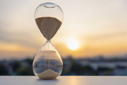 Hourglass with sand flowing at sunset. Could symbolize that time is fleeting, New Year reflections, countdowns, resolutions, and time concept backgrounds.