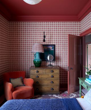 Bedroom with red patterned wallpaper and red celing and orange armchair and armoire