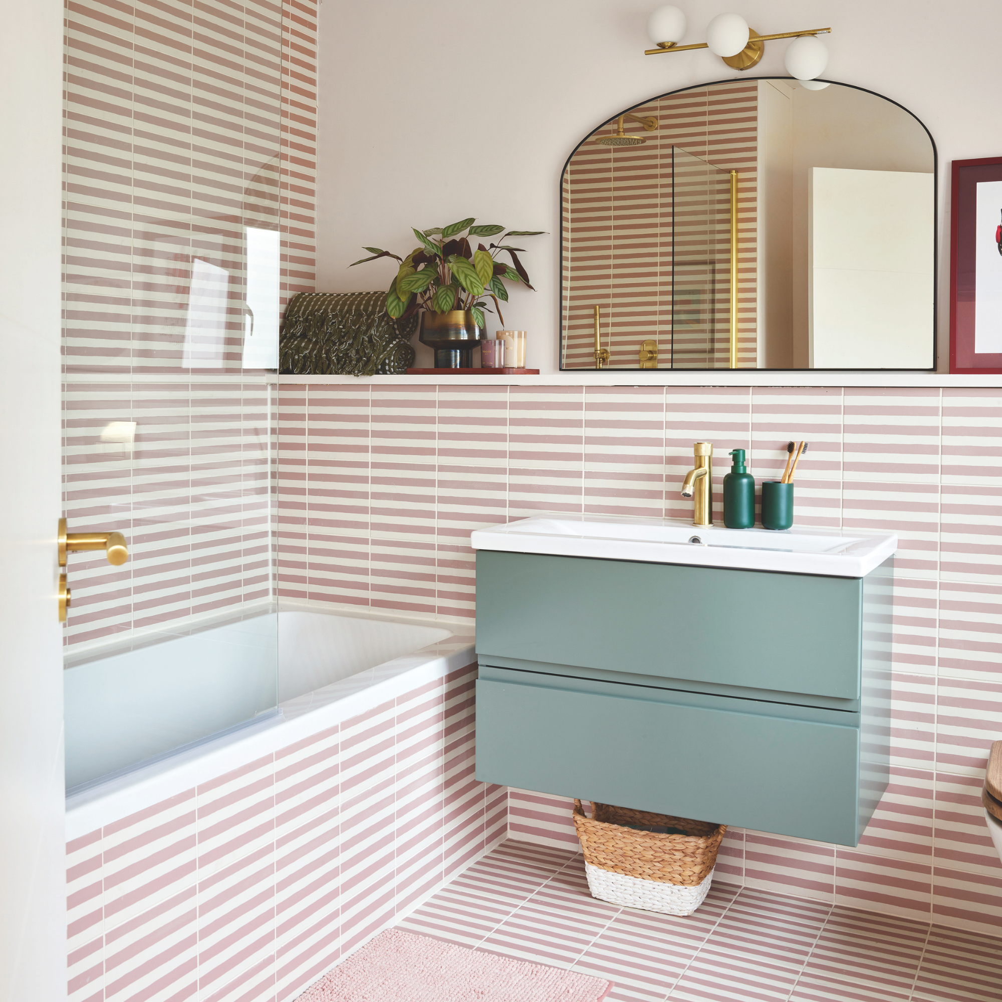Pink and white stripe tiled bathroom with blue sink and brass finishes.