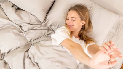 A woman smiling and stretching while lying in bed with Luff Sleep sheets