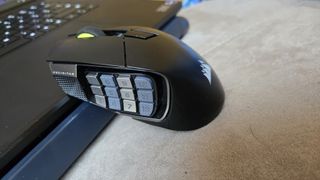 A Corsair Scimitar Elite Wireless SE gaming mouse on a carpet next to a gaming laptop and Stream Deck.