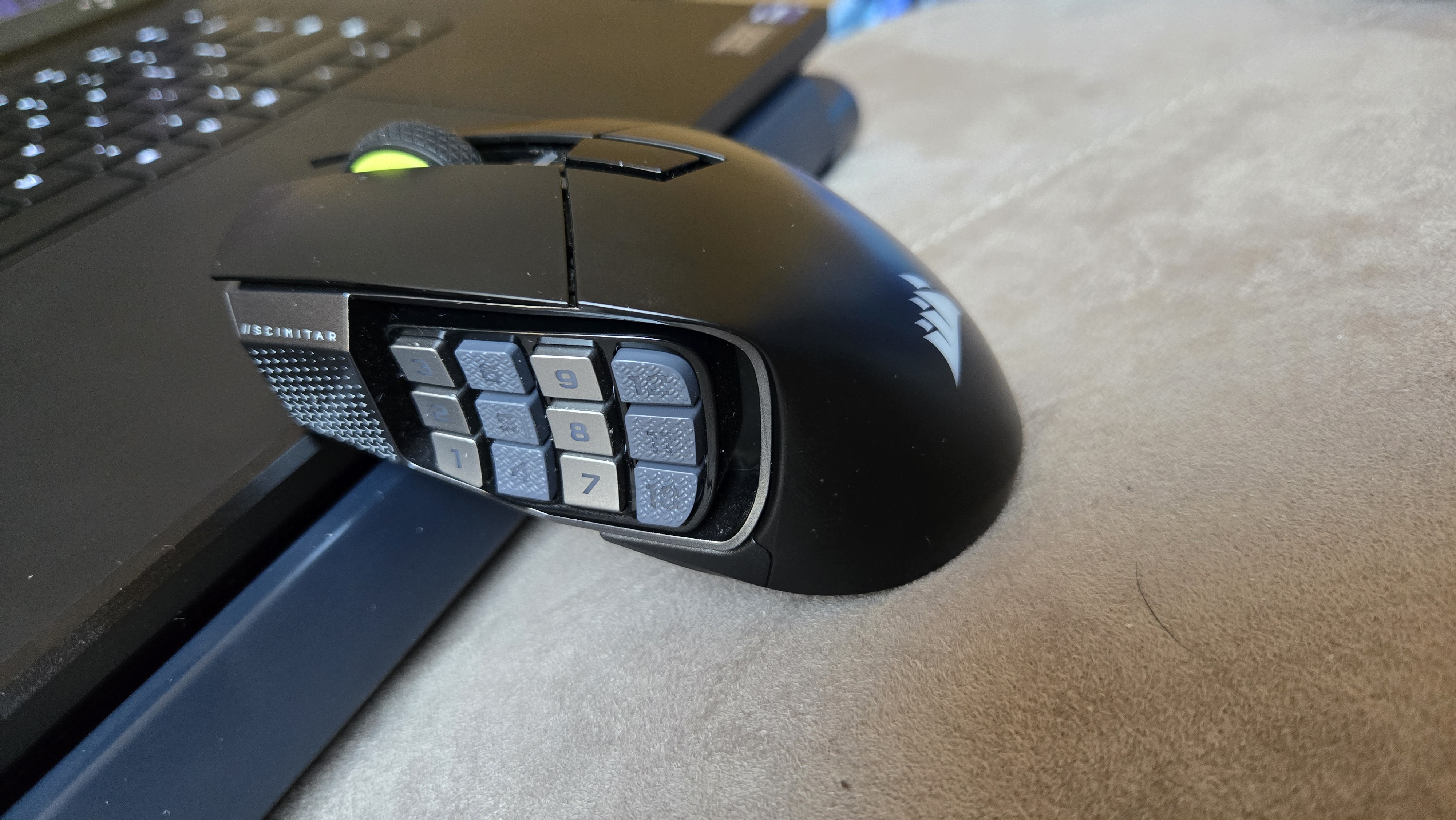 A Corsair Scimitar Elite Wireless SE gaming mouse on a carpet next to a gaming laptop and Stream Deck.