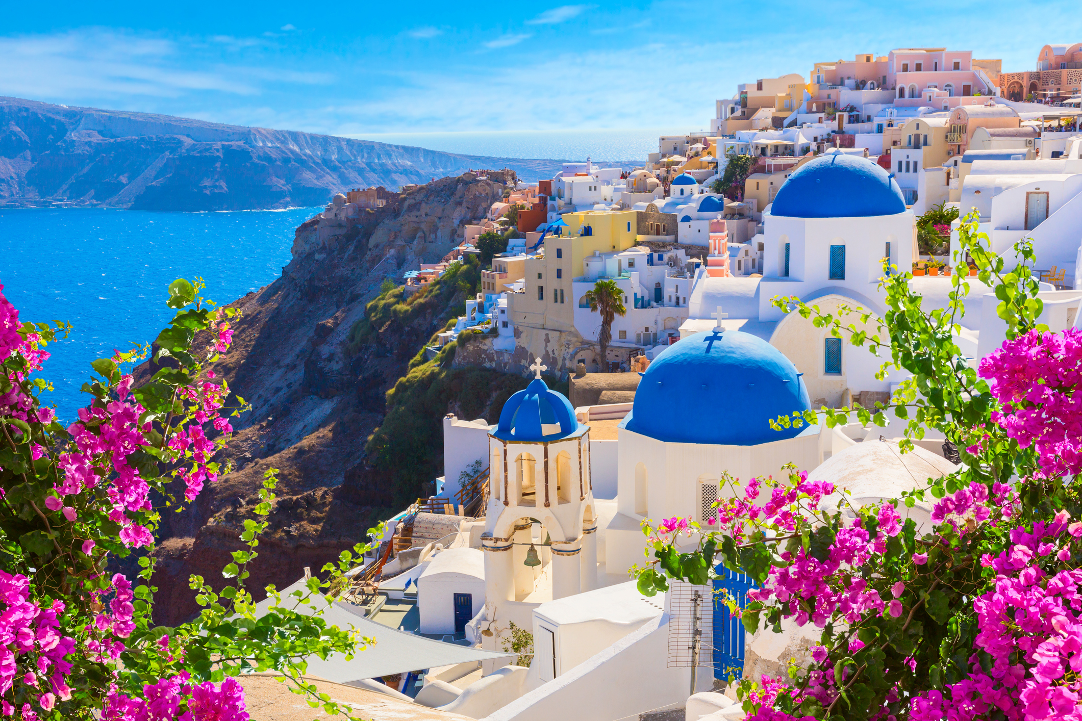 a view of Santorini island, with its traditional white houses and churches with blue domes over the Caldera and Aegean Sea.