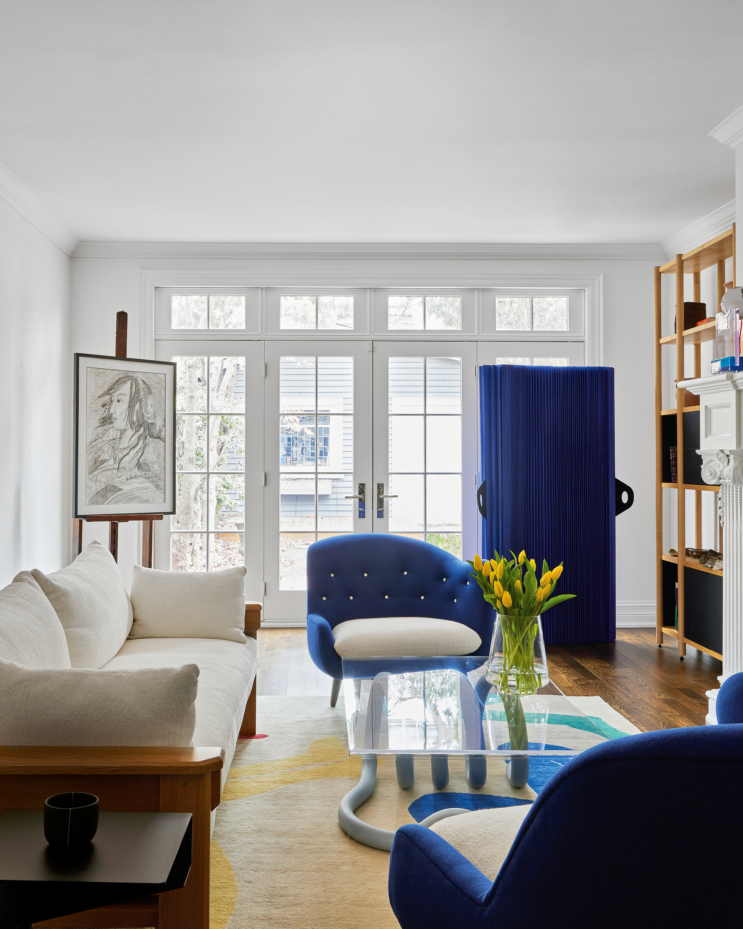 White living room with patio doors to garden, cream sofa, cobalt blue cabinet and armchairs, and glass coffee table