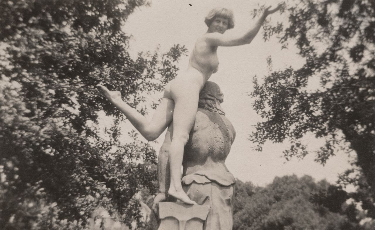 black and white photograph of nude woman (Dora Carrington)posing on top of statue