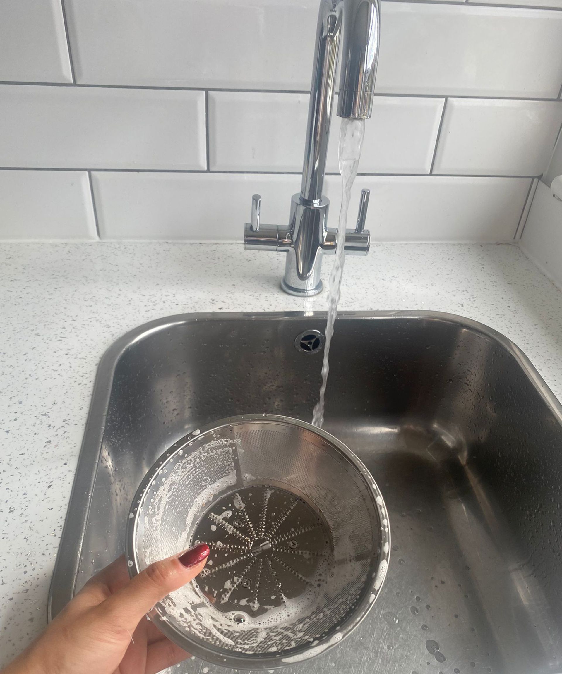 Christina Chrysostomou membersihkan komponen layar Nutribullet Juicer Pro dengan sabun cuci piring dan air mengalir di dapur berubin putih