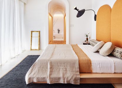 A bedroom with white walls and yellow accents facing a large floor to ceiling window with a voile curtian